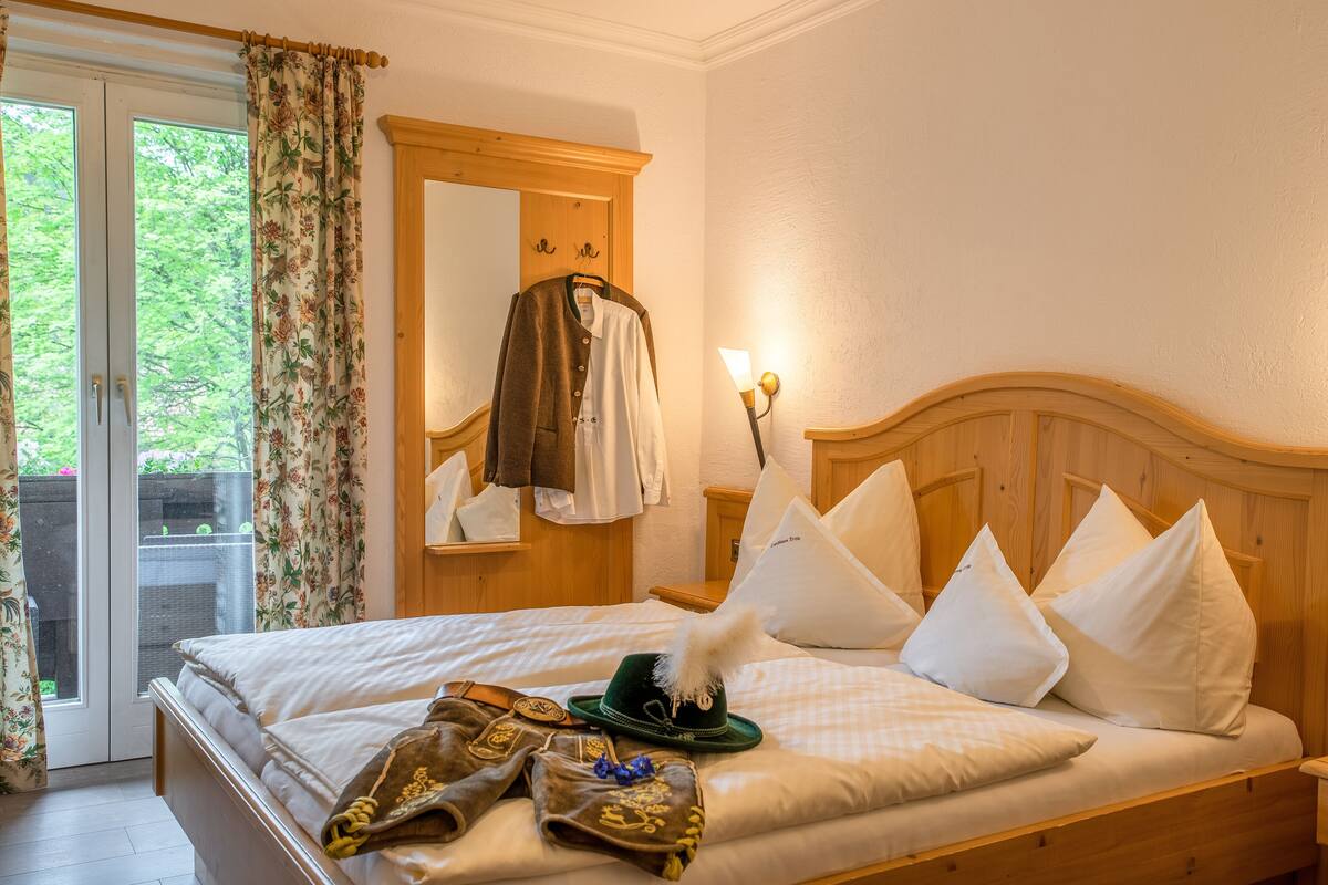 A bedroom with a bed, pillows, a hat, and a coat on the wall.