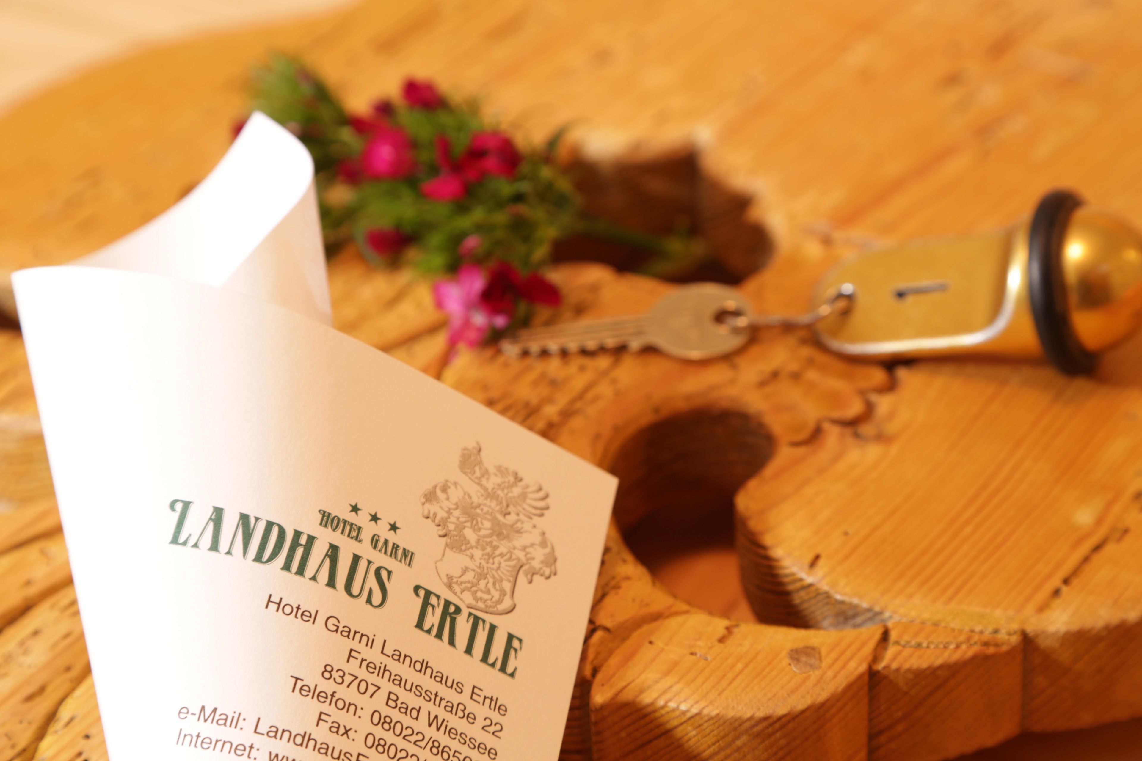 A hotel brochure titled "Landhaus Ertle" with contact information and a wooden table with a key and flowers.