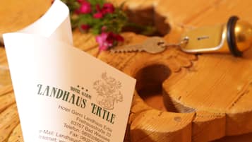Un folleto de hotel titulado "Landhaus Ertle" con información de contacto y una mesa de madera con una llave y flores.