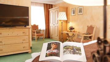 Une chambre d’hôtel équipée d’une télévision, d’une commode en bois, de deux chaises, d’une table avec une lampe et d’un livre posé sur le lit.