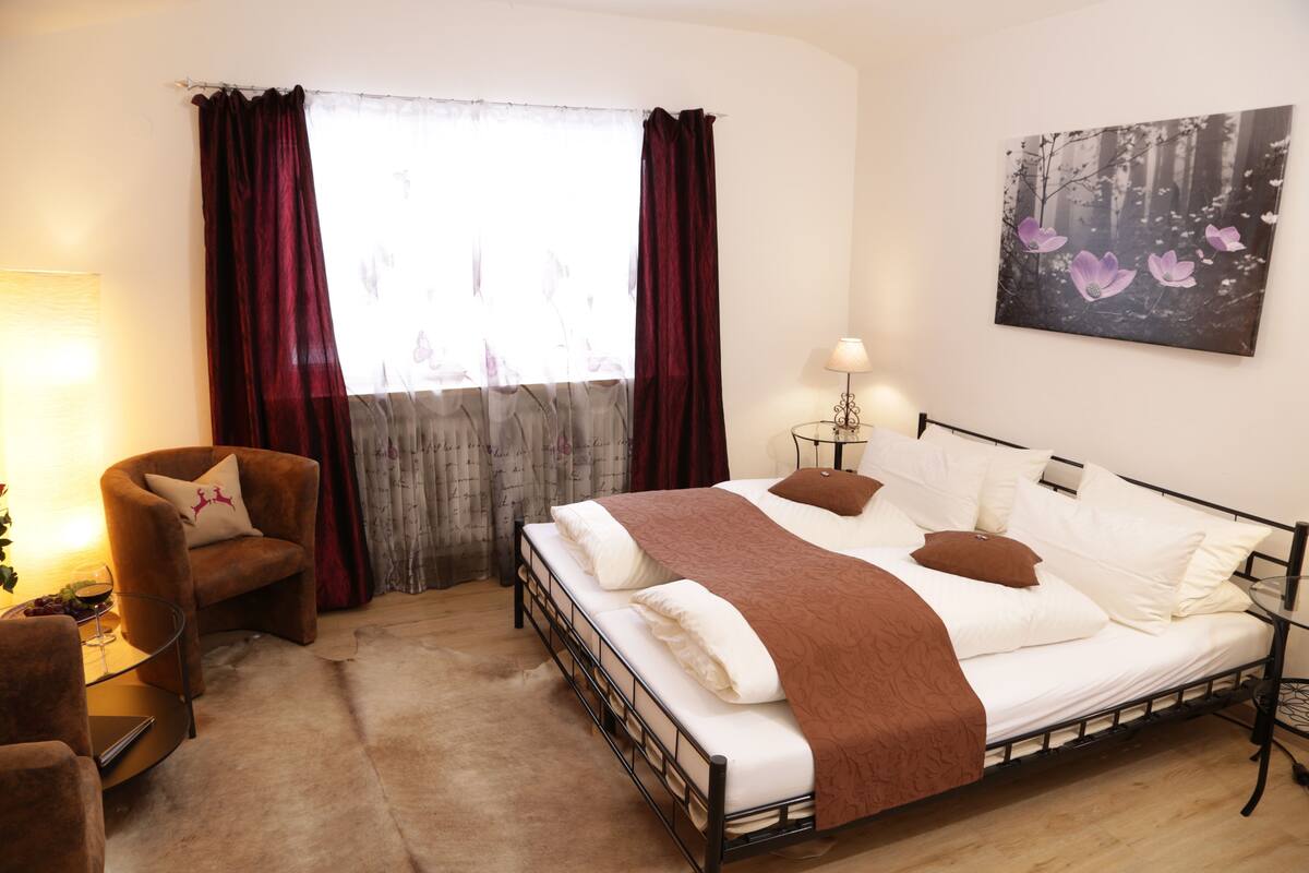 A bedroom with a bed, a chair, a lamp, and a painting on the wall.