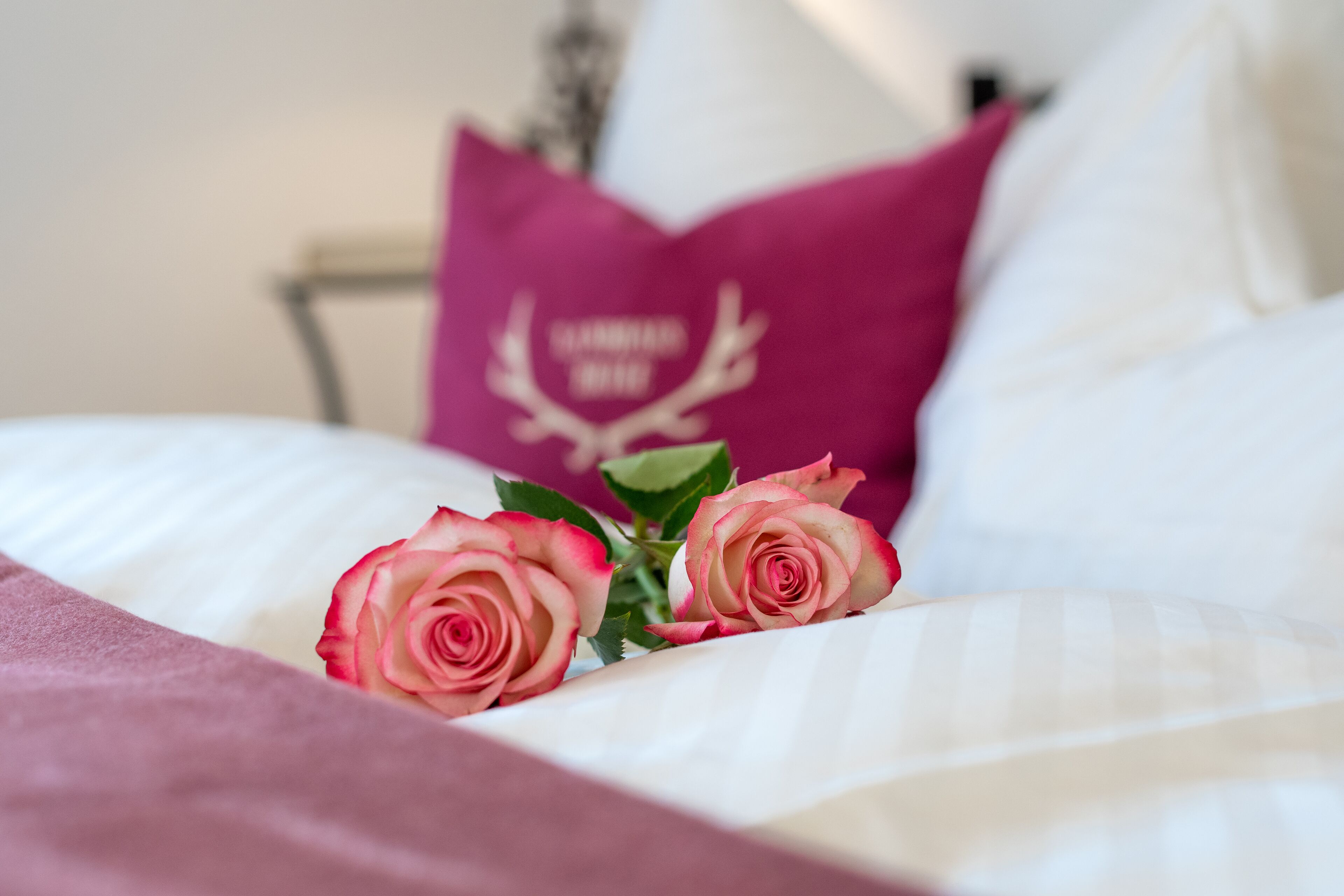 Ein Bett mit rosa Rosen und einem Kopfkissen mit einem Hirsch-Logo.