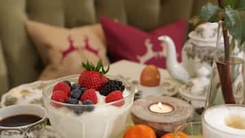 A table setting with a dessert bowl of yogurt topped with berries, a teapot, a candle, and a cup of coffee.