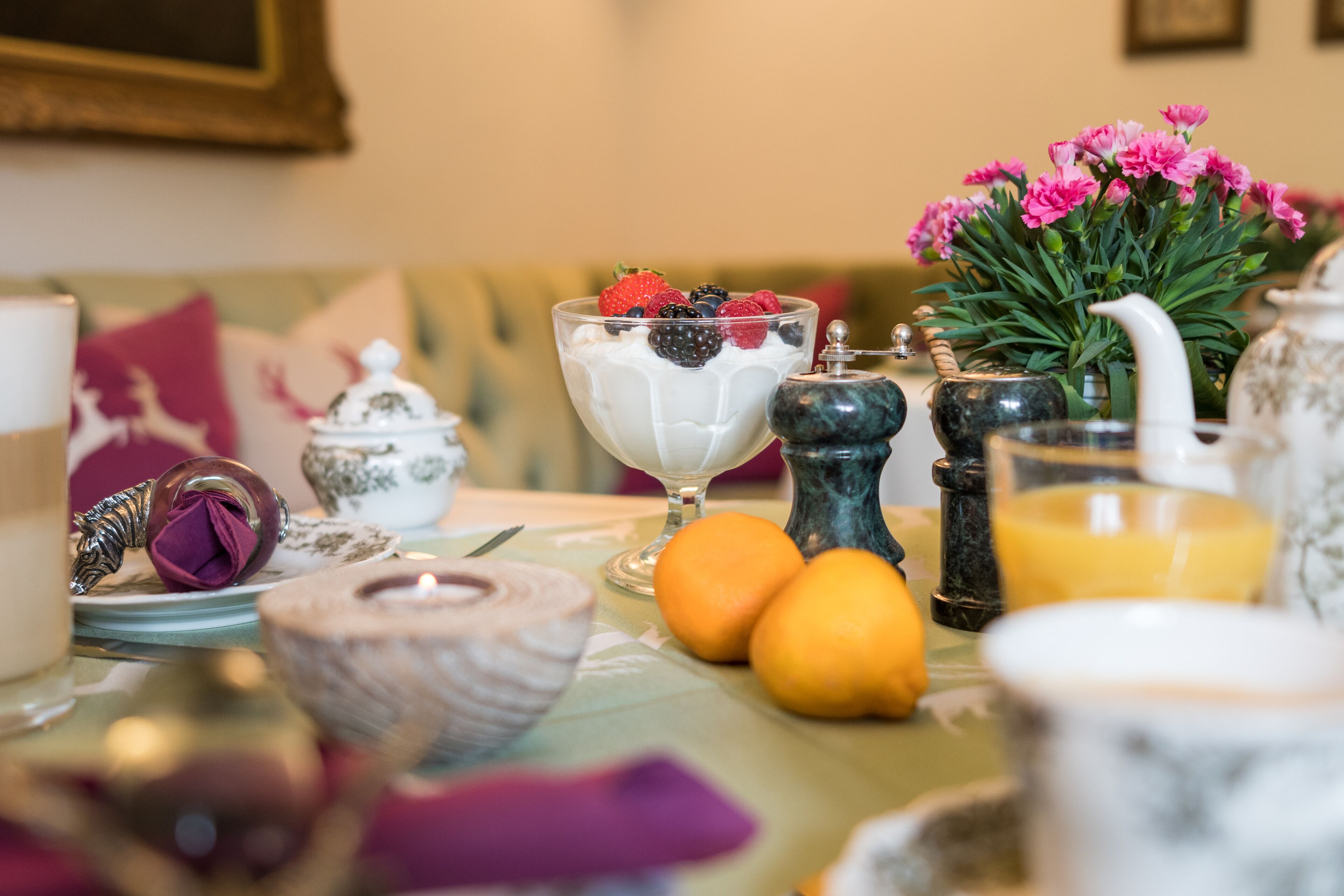A table set with a dessert, fruits, and a vase of flowers.
