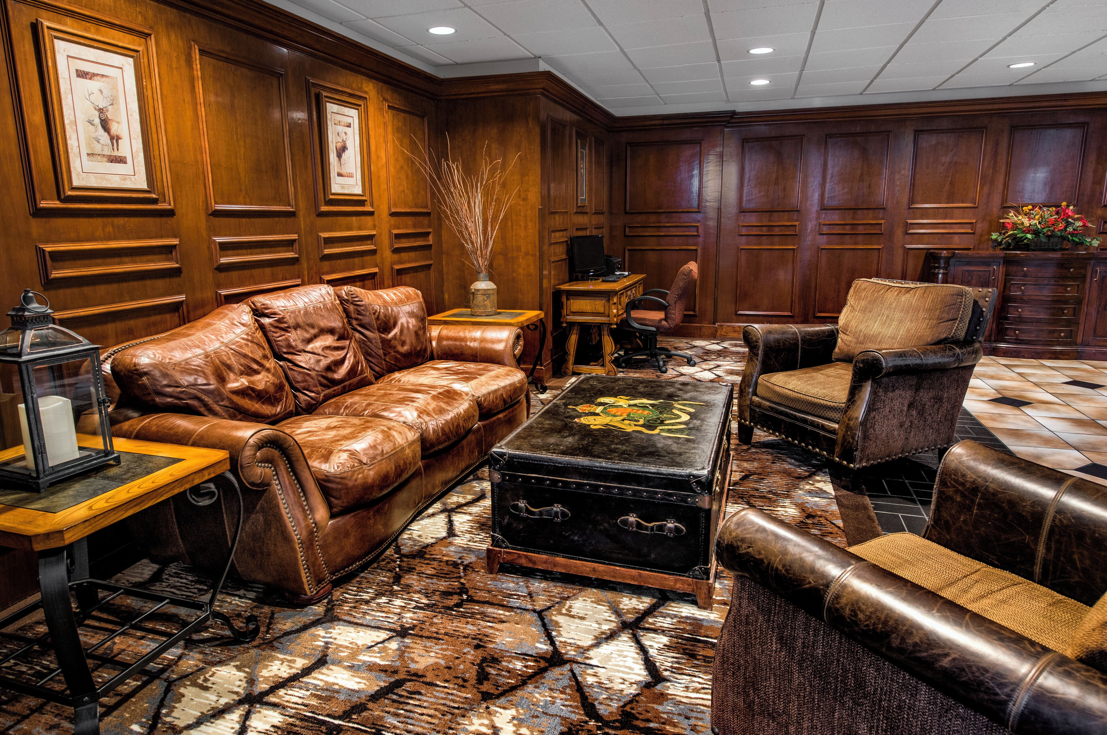 A leather sofa, a matching armchair, a small table, and a decorative trunk in a room with wooden paneling and a patterned carpet.