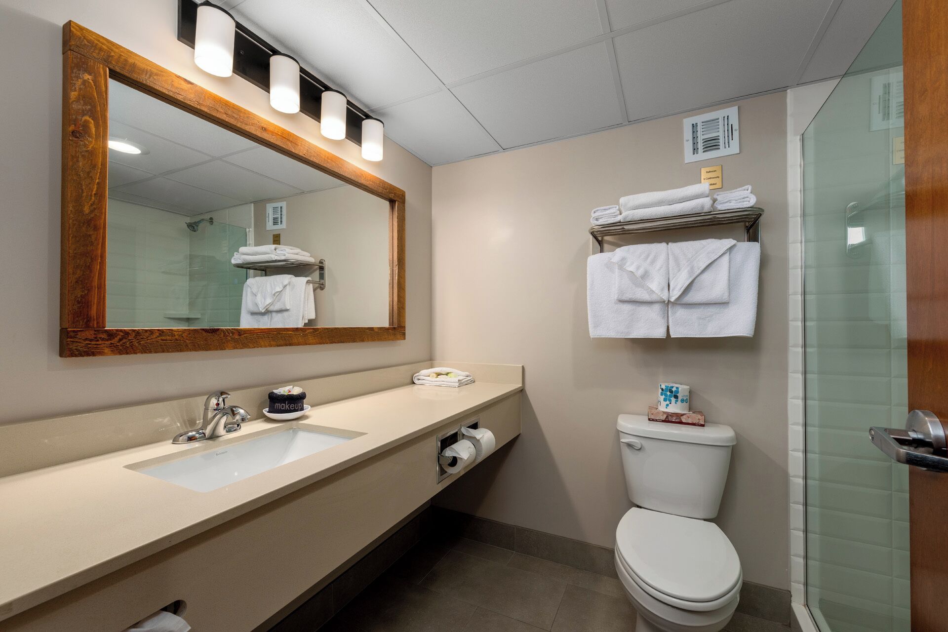 Une salle de bain avec un grand miroir, un lavabo, des toilettes et une douche à parois de verre.