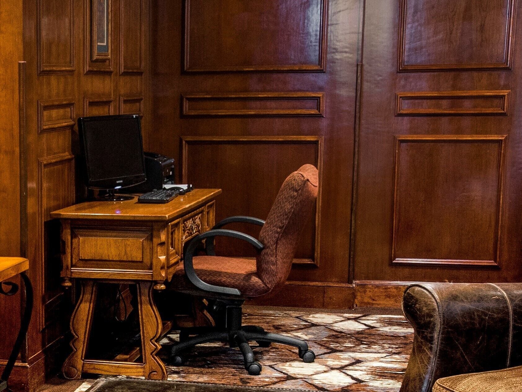 Een houten bureau met een computer en toetsenbord, een bruine bureaustoel en een vloer met een patroon.