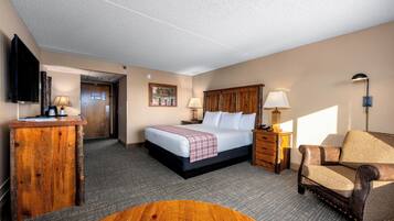 A hotel room with a bed, a desk, a chair, a lamp, and a television.