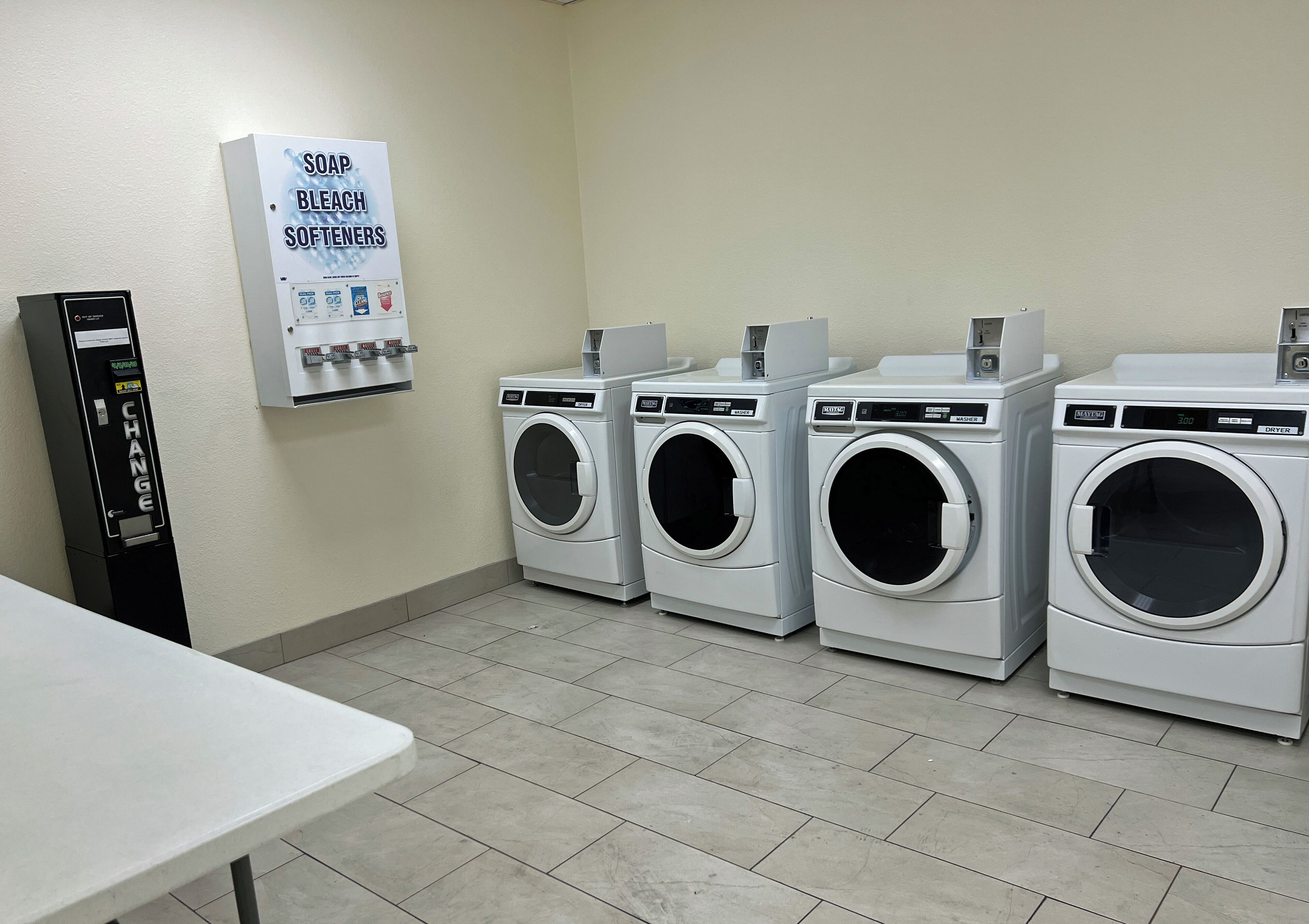 A laundry room with four washing machines and a change machine.