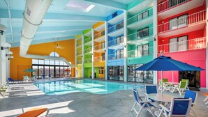 Zona interior de piscina con varios niveles, una piscina central, múltiples áreas de descanso con sombrillas y vistas de los edificios circundantes.