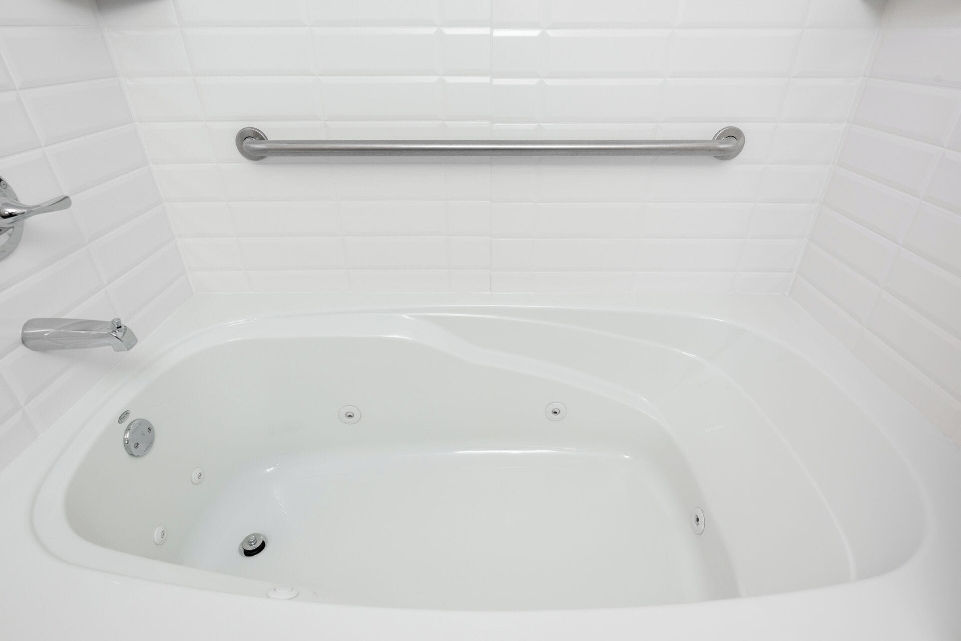 Una vasca da bagno bianca con maniglia di sostegno, rubinetteria e scarico.