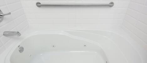 Una vasca da bagno bianca con maniglia di sostegno, rubinetteria e scarico.