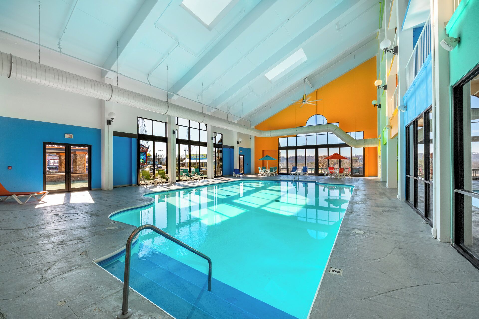 An indoor swimming pool with clear glass walls, a blue floor, and a bright orange ceiling.