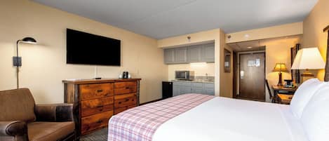 A hotel room with a bed, a dresser, a TV, a desk with a lamp, and a kitchenette.