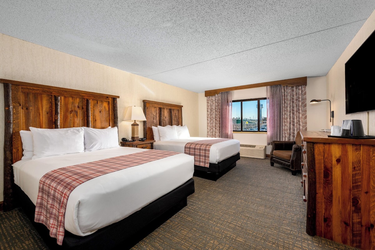 A hotel room with two beds, a desk, a chair, a television, and a window with a view.