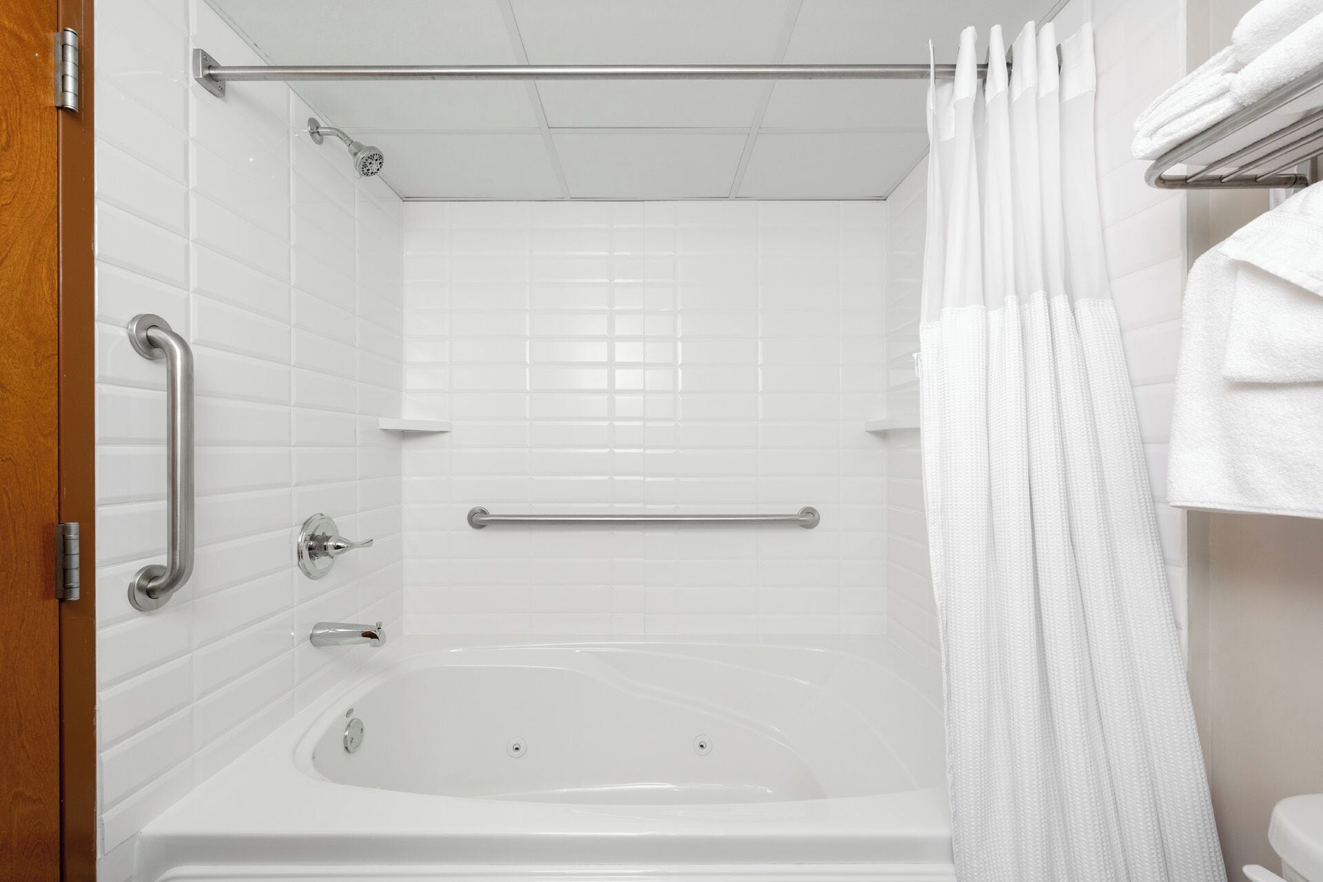 A bathroom with a bathtub, grab bars, a shower curtain, and a towel rack.