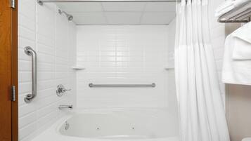 Un baño con bañera, barras de apoyo, cortina de ducha y un perchero para toallas.