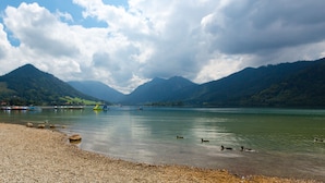 A lake with mountains in the background, a pebbled shore, and a few boats. - Karma Bavaria (Schliersee)
