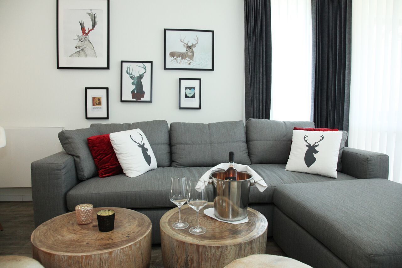 Un salon moderne avec un canapé d’angle gris, deux petites tables basses rondes en bois et des œuvres d’art encadrées représentant des animaux sauvages accrochées au mur.