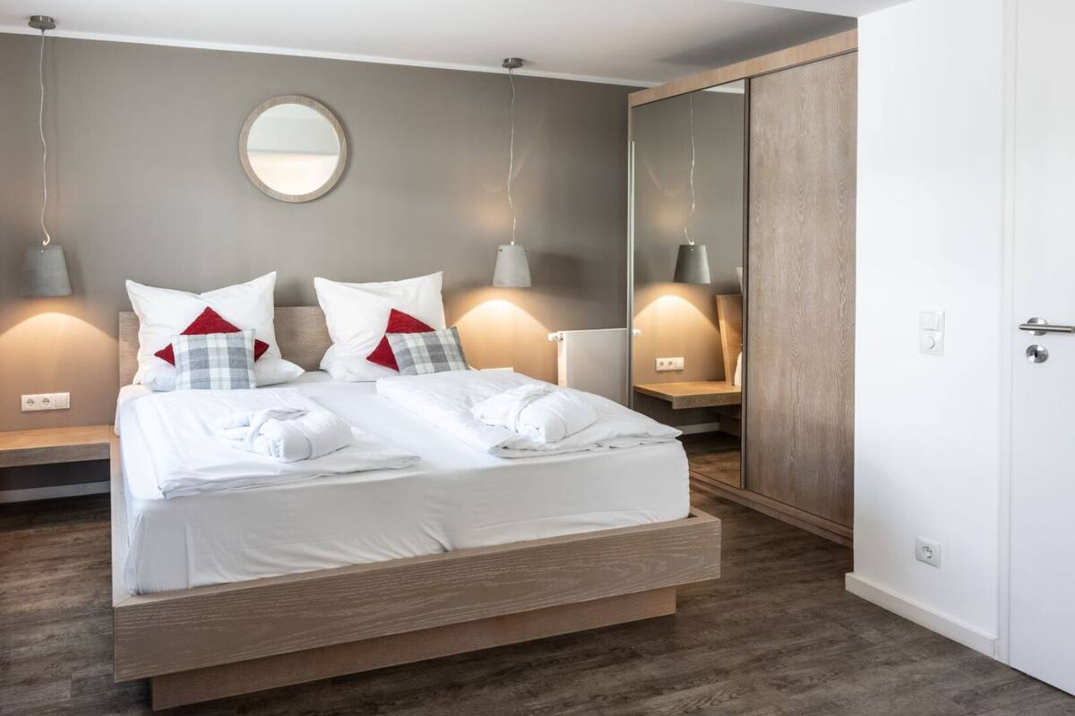 Quarto de hotel moderno com uma cama grande, abajures, um espelho redondo e um guarda-roupa.