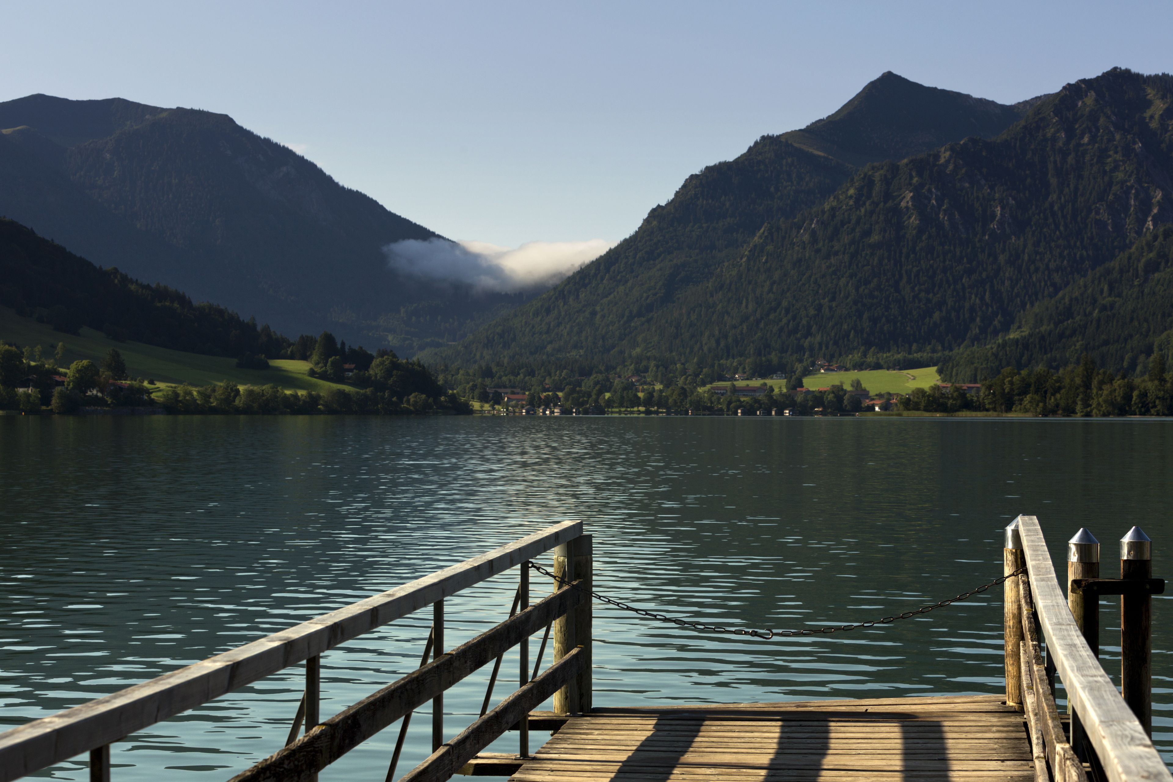 Un muelle de madera se adentra en un lago tranquilo con montañas al fondo.