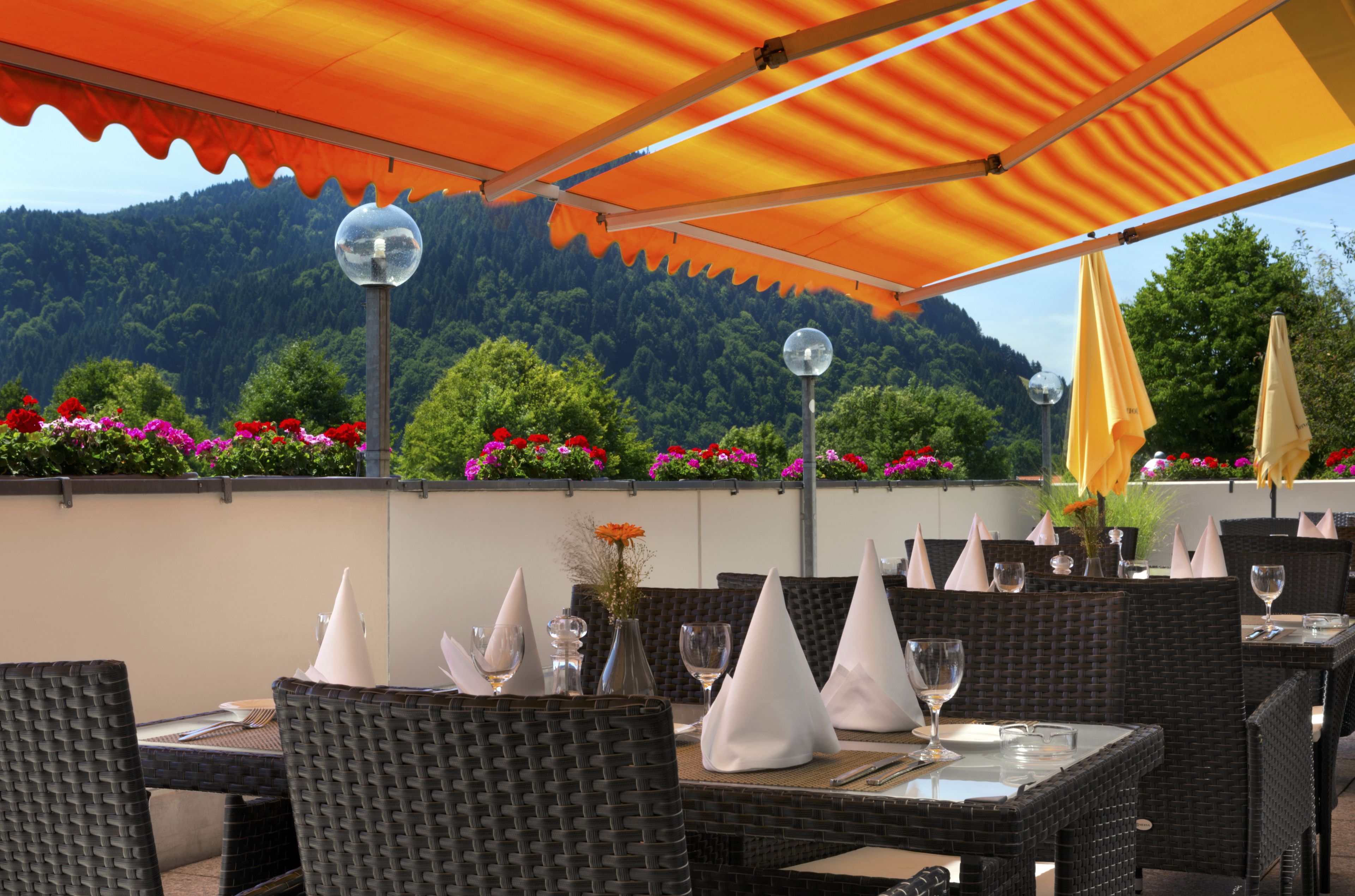 An outdoor dining area with wicker furniture, white napkins, and a mountain backdrop.