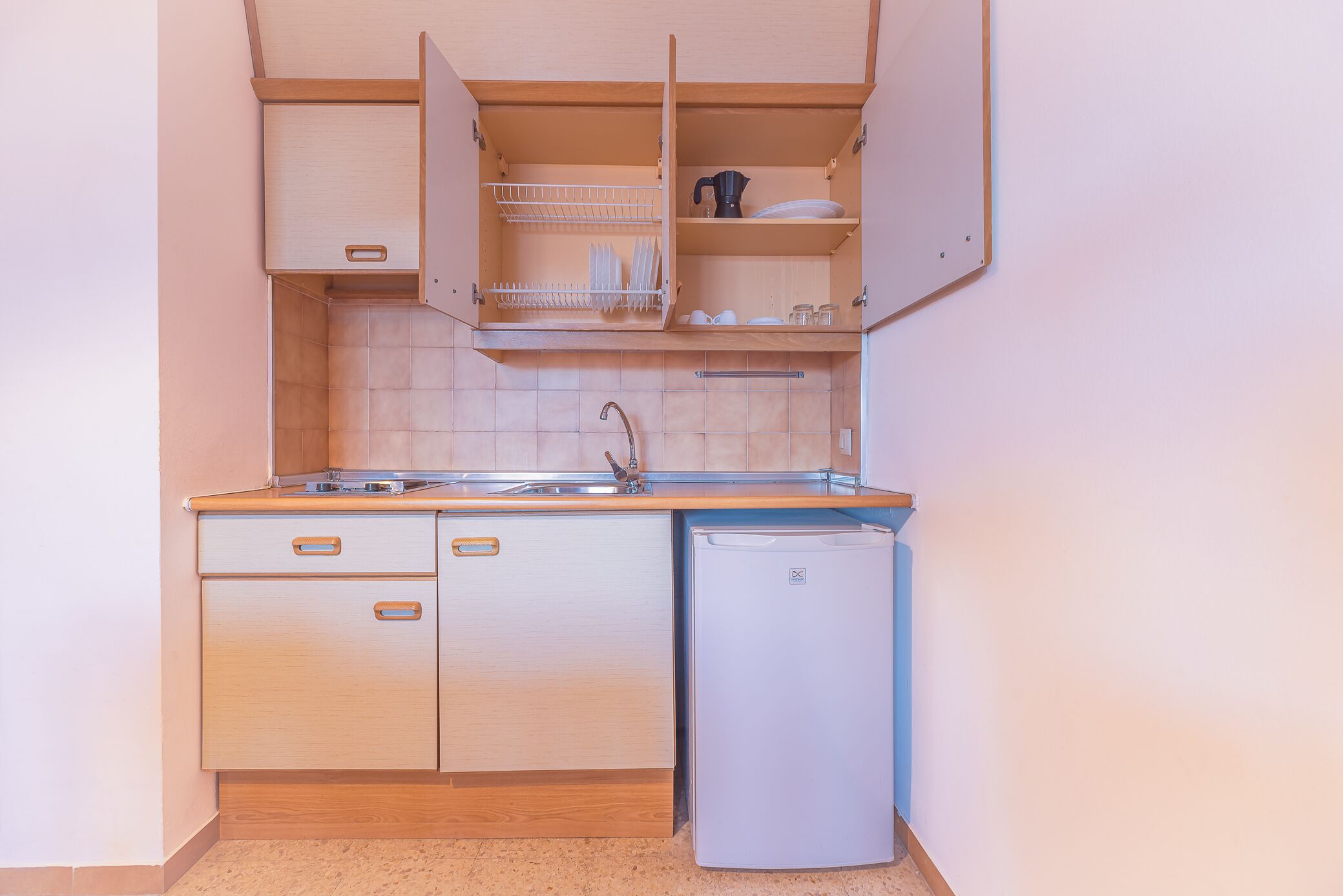 Una cocina compacta con armarios de madera, un lavamanos y un refrigerador pequeño.