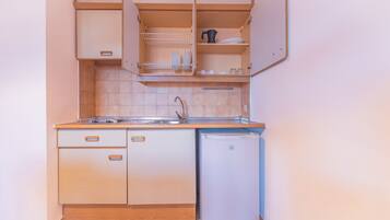 Una cocina compacta con armarios de madera, un lavamanos y un refrigerador pequeño.