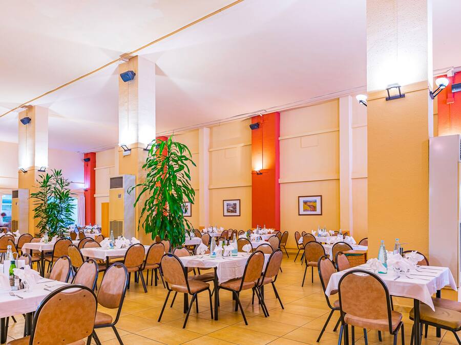 A large dining hall with multiple tables and chairs, arranged in rows.