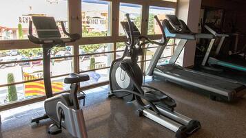 Un gimnasio con bicicletas estáticas, cintas de correr y una ventana que ofrece vistas a coches estacionados y edificios.