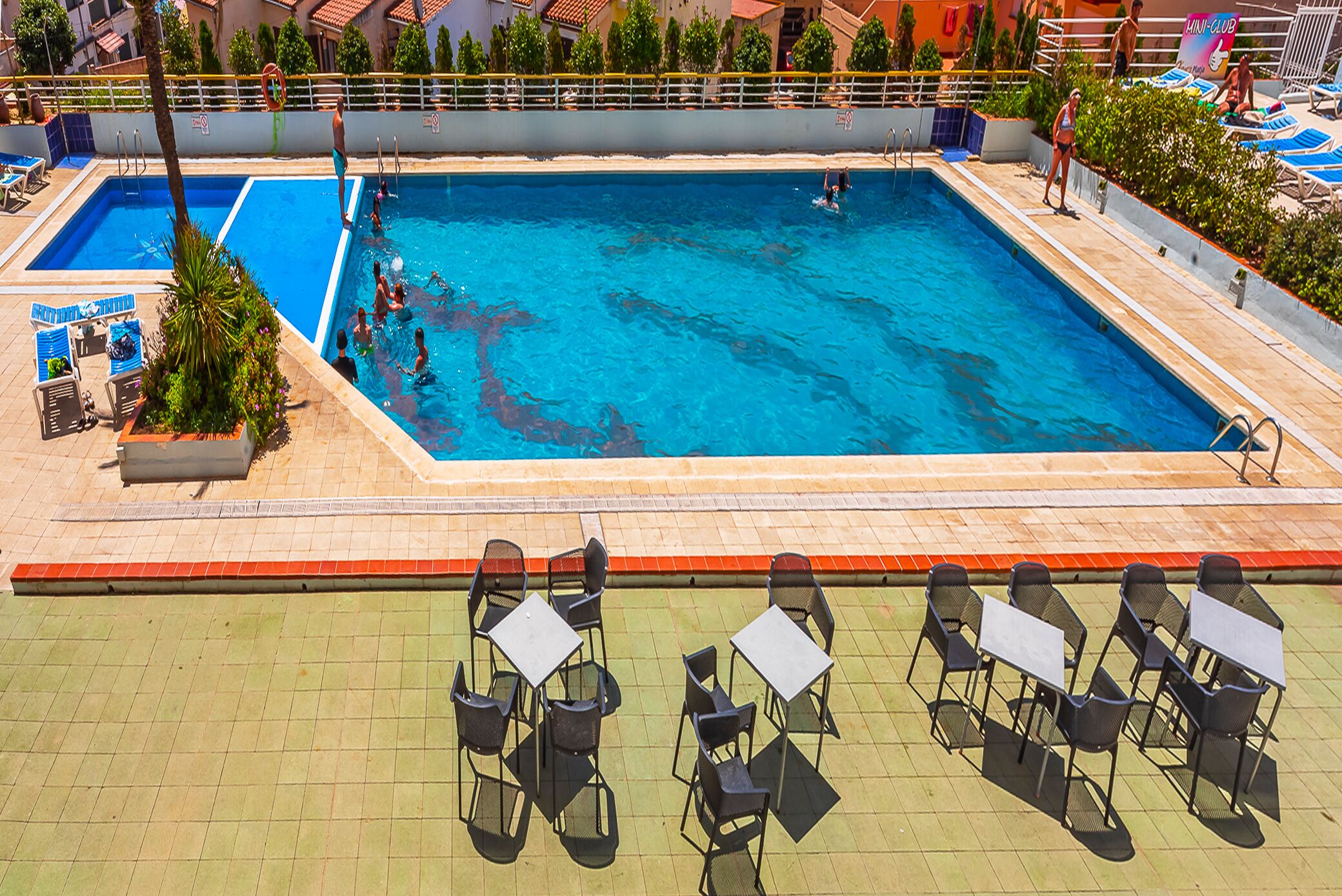 Une piscine dotée de plusieurs couloirs, de chaises longues et de tables disposées tout autour.