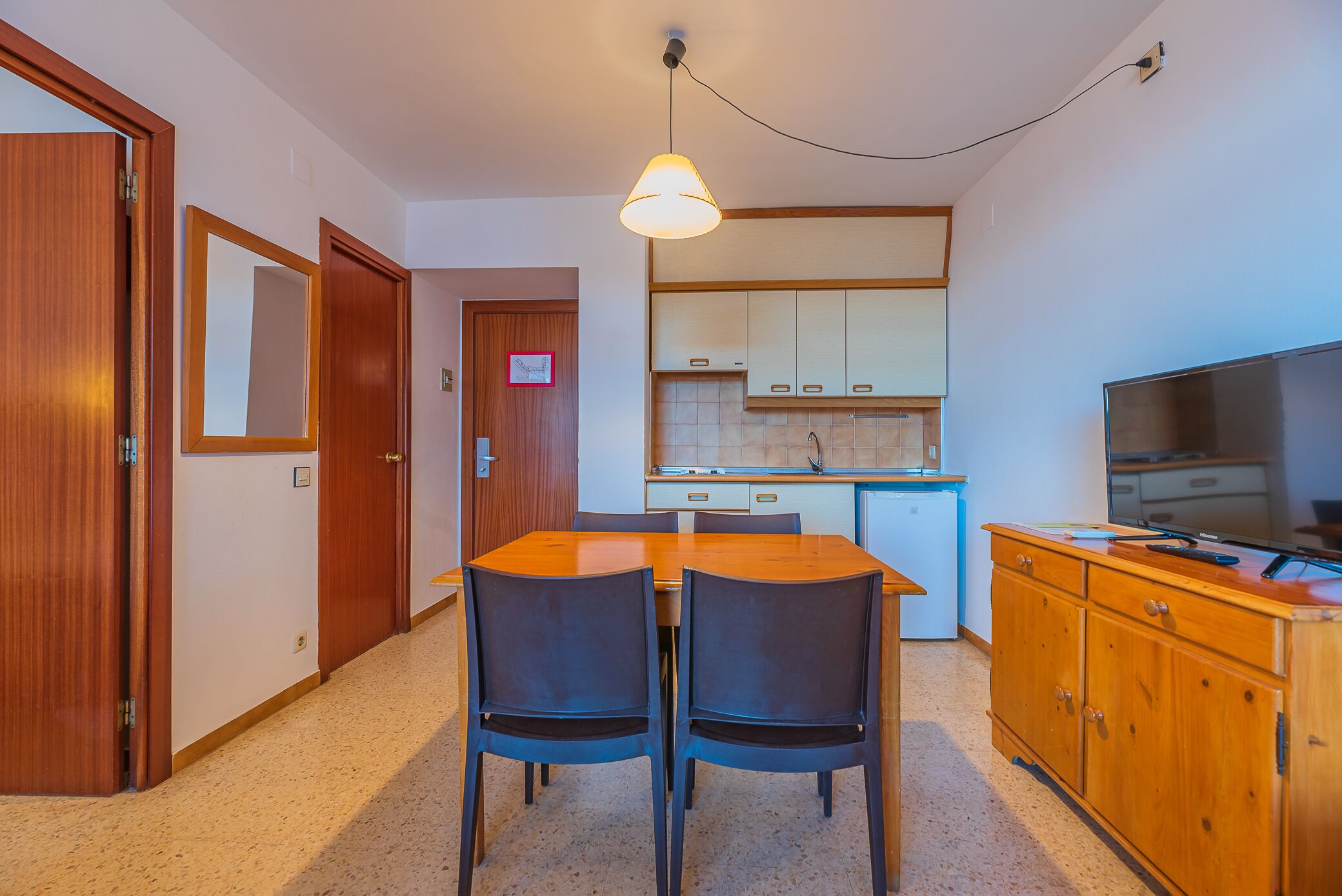 A compact kitchen with a dining area, wooden cabinets, a TV, and a small refrigerator.