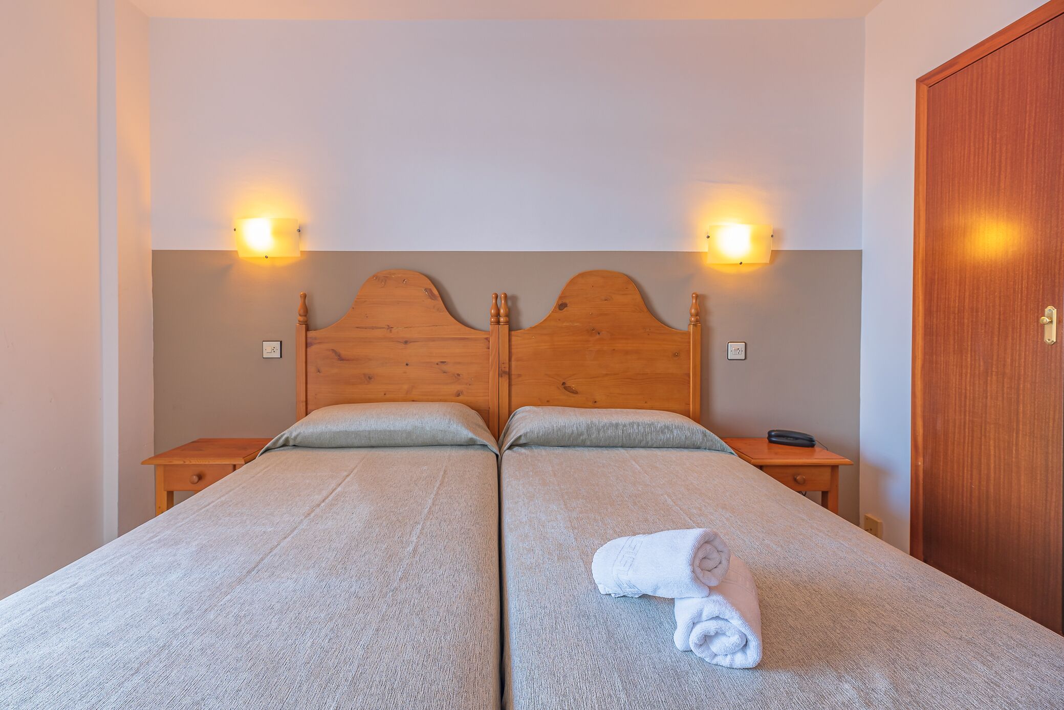 Una cama doble con cabecera de madera, dos mesitas de noche y un armario de madera.