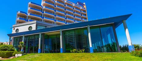 A modern hotel with a glass facade, multiple balconies, and a well-maintained lawn.