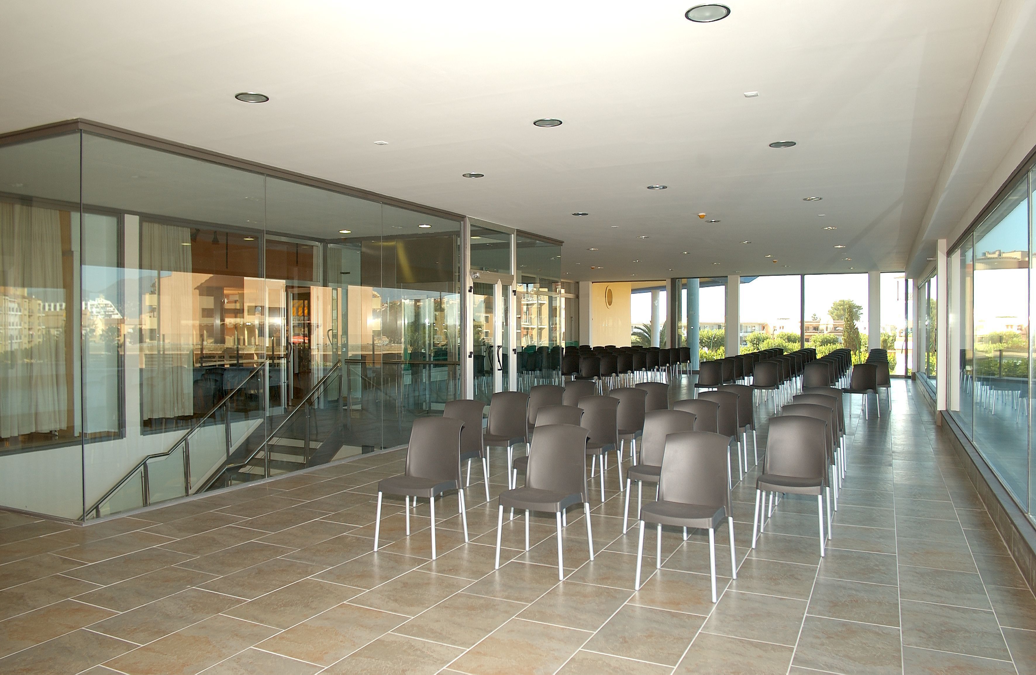 A spacious indoor area with a long row of chairs, a staircase, and large windows offering a view of the outside.