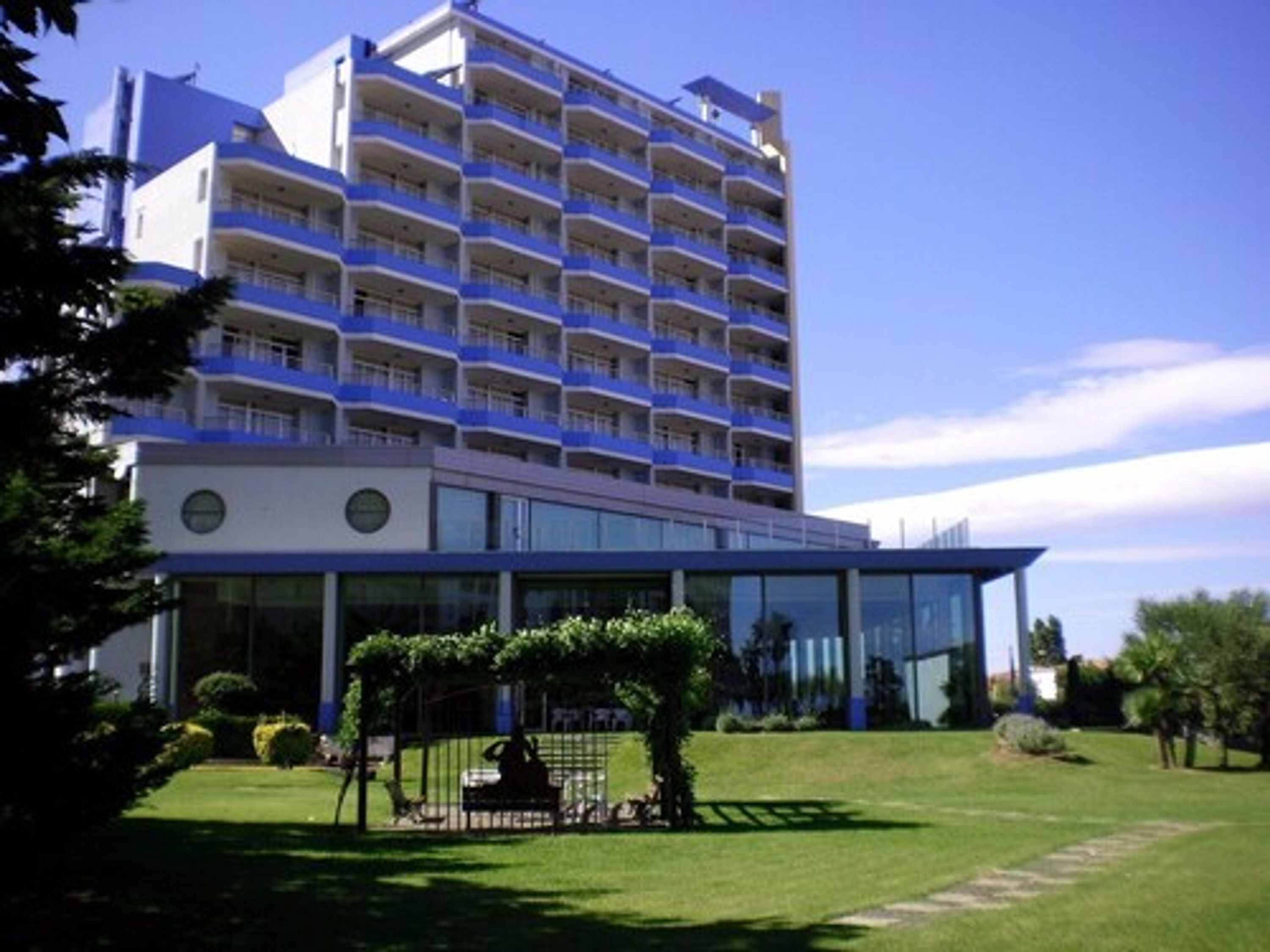 A multi-story hotel with a modern design, featuring balconies on each floor and a glass facade.