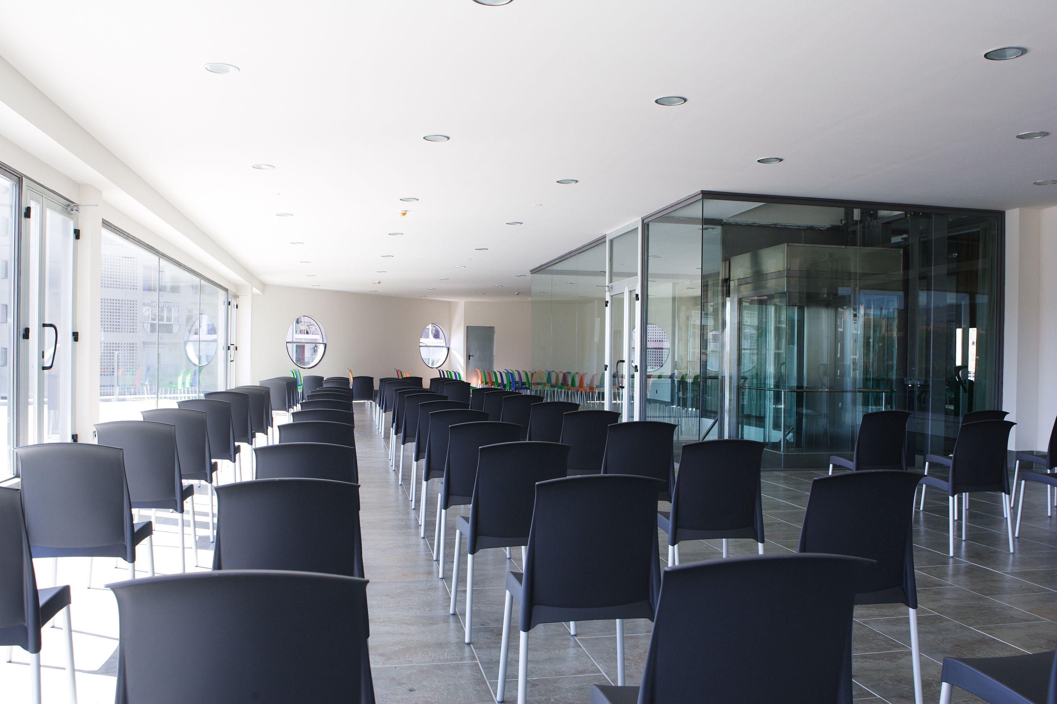A conference room with rows of black chairs, large windows, and a glass wall.