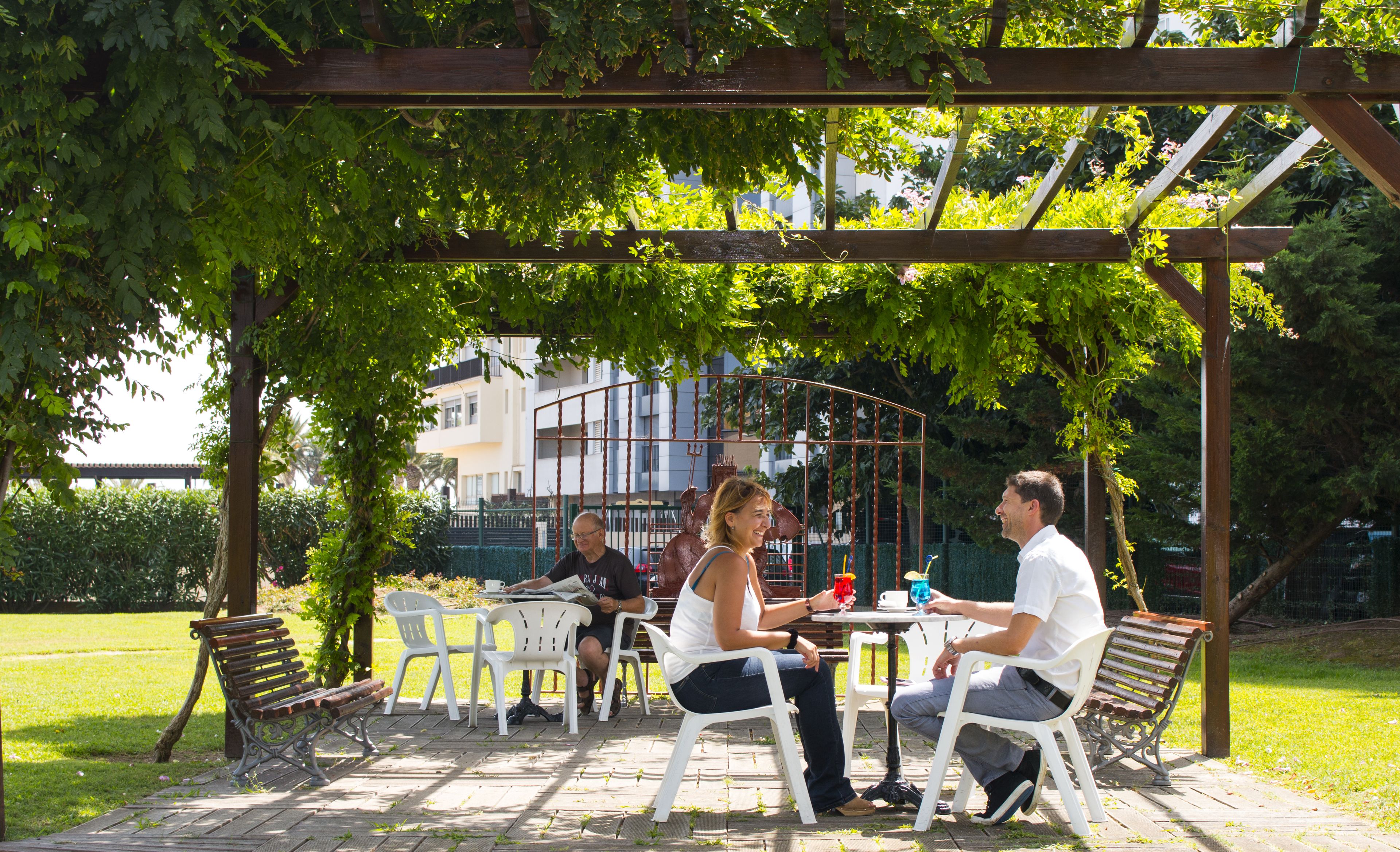 An outdoor patio area with a pergola, white plastic chairs, and tables.