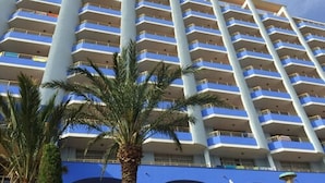 Un hôtel de grande hauteur doté de nombreux balcons, bordé de palmiers et surplombant un ciel d’un bleu éclatant.
