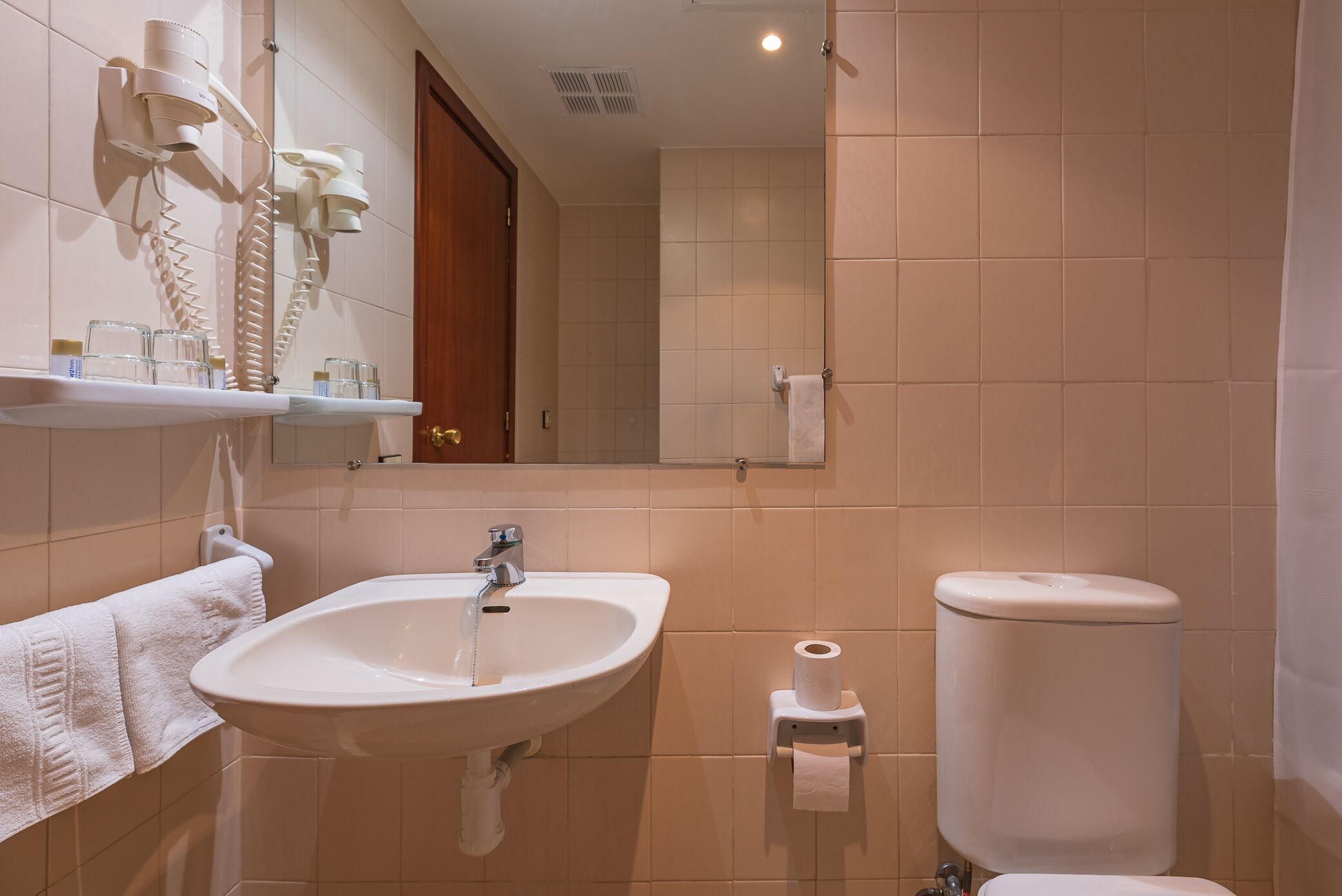 A bathroom with a sink, mirror, towel rack, toilet, and a hairdryer mounted on the wall.