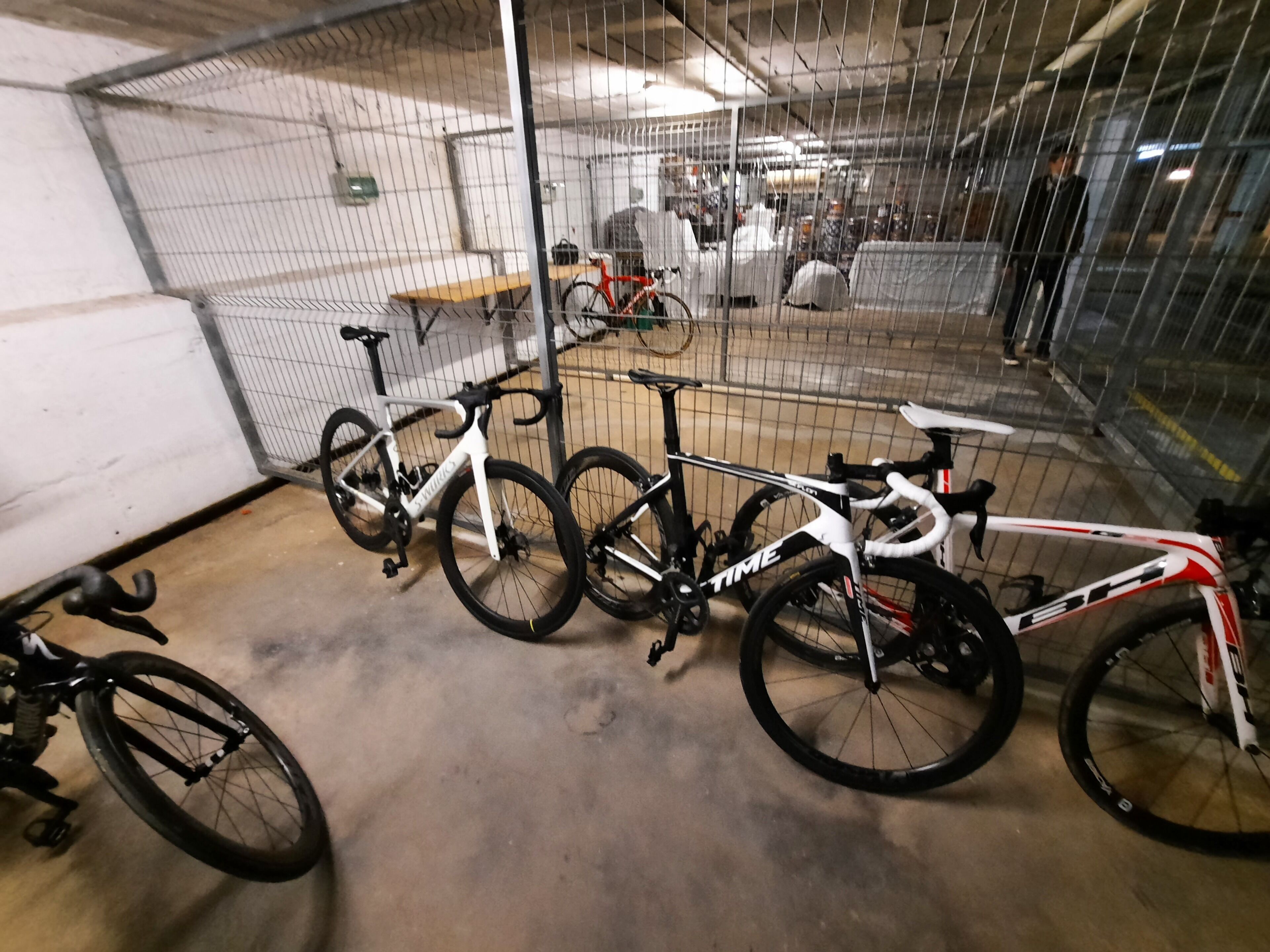 Un área de almacenamiento de bicicletas segura, con valla metálica, suelo de hormigón y varias bicicletas.
