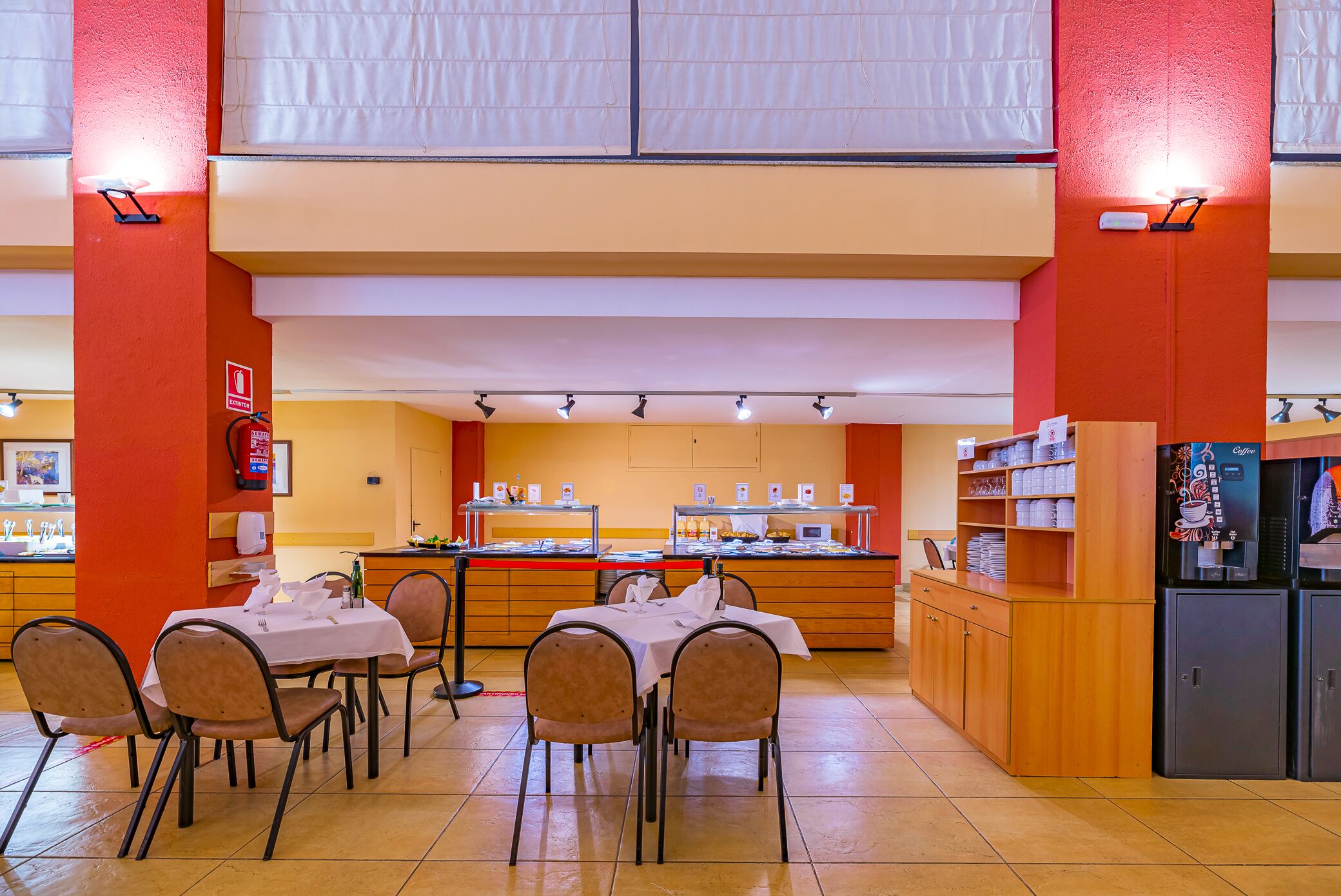 A restaurant with a high ceiling, a counter with a coffee machine, and a buffet area.