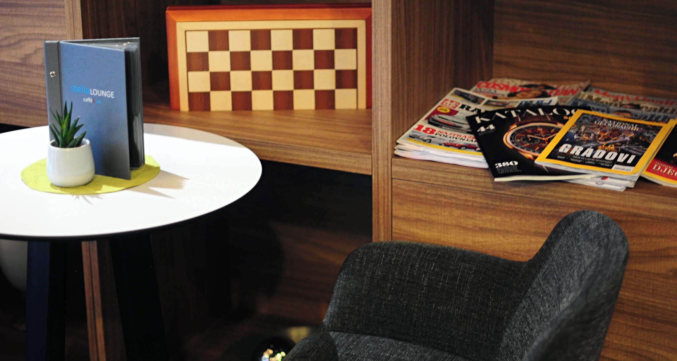 Une pièce avec une table ronde, une chaise, une petite plante en pot, un panneau mural à carreaux et des magazines sur la table.