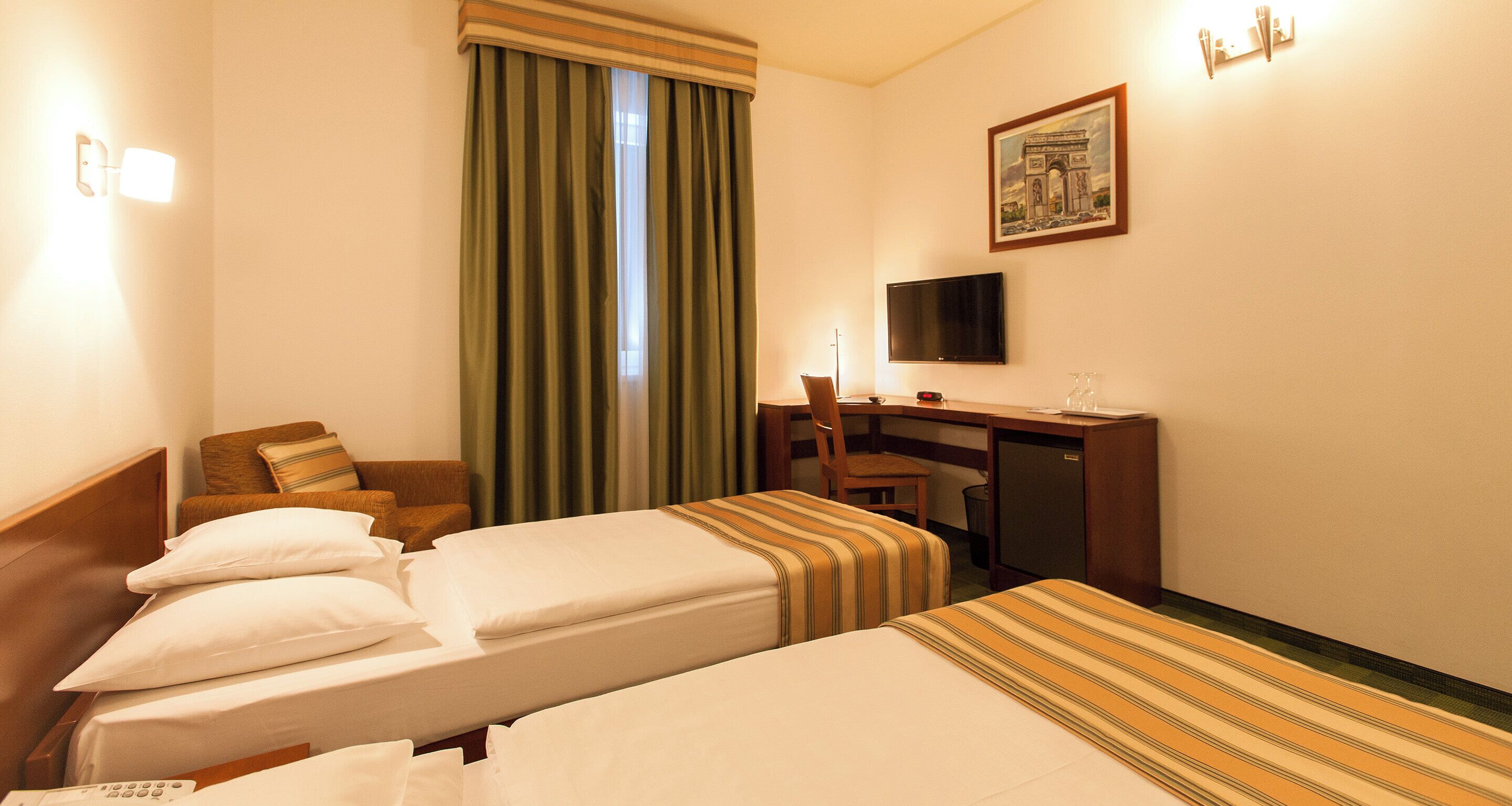 A hotel room with two beds, a desk, a chair, a television, and a window with curtains.