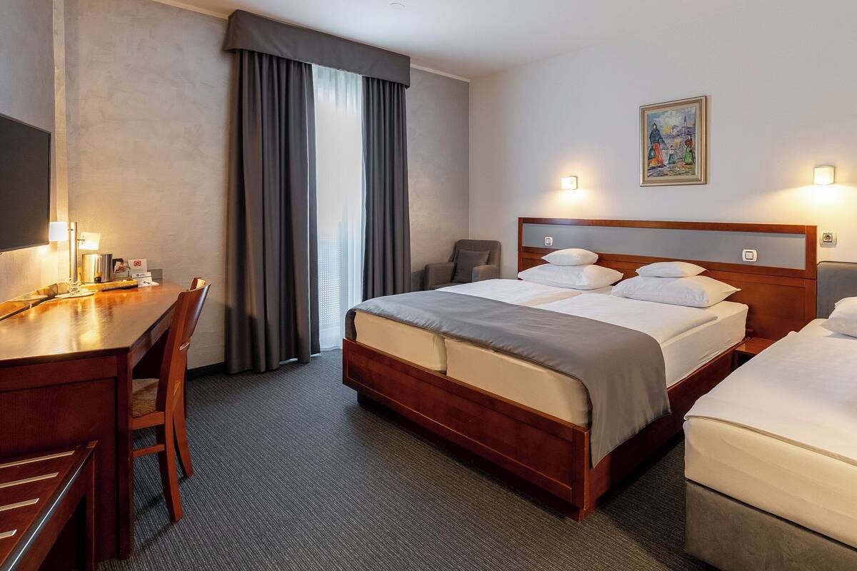 A hotel room with two beds, a desk, a chair, a television, and a painting on the wall.