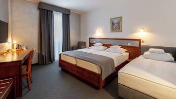 A hotel room with two beds, a desk, a chair, a television, and a painting on the wall.