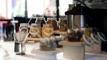 Esposizione di diversi alimenti in vasetti con cucchiaini, una macchina del caffè e un piccolo contenitore metallico con utensili.
