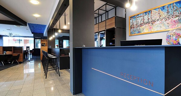 A modern reception area with a blue reception desk labeled "RECEPTION," a bar area, and a terrace visible in the background. - Best Western Airport Hotel Stella (Zagreb)