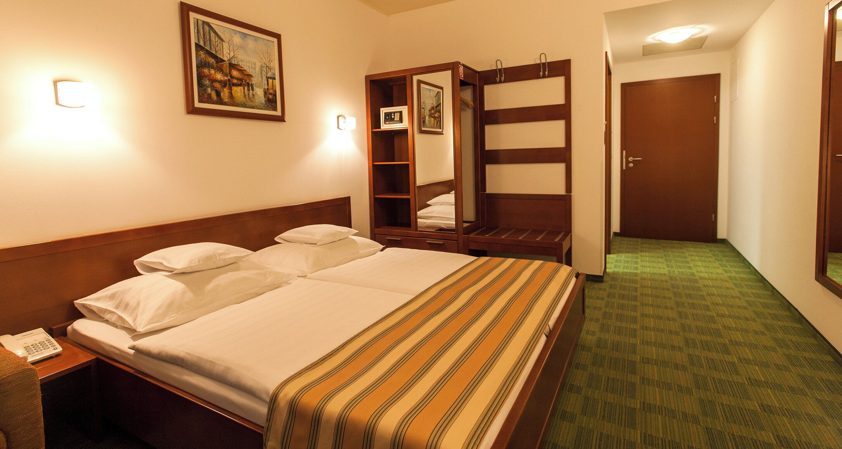 Habitación de hotel con cama, mesita de noche con teléfono, espejo, armario y puerta.