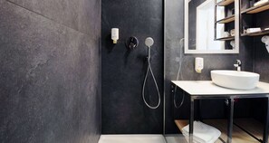 A modern bathroom with a dark tiled wall, a white sink, and a shower with a handheld showerhead. - Best Western Airport Hotel Stella (Zagreb)